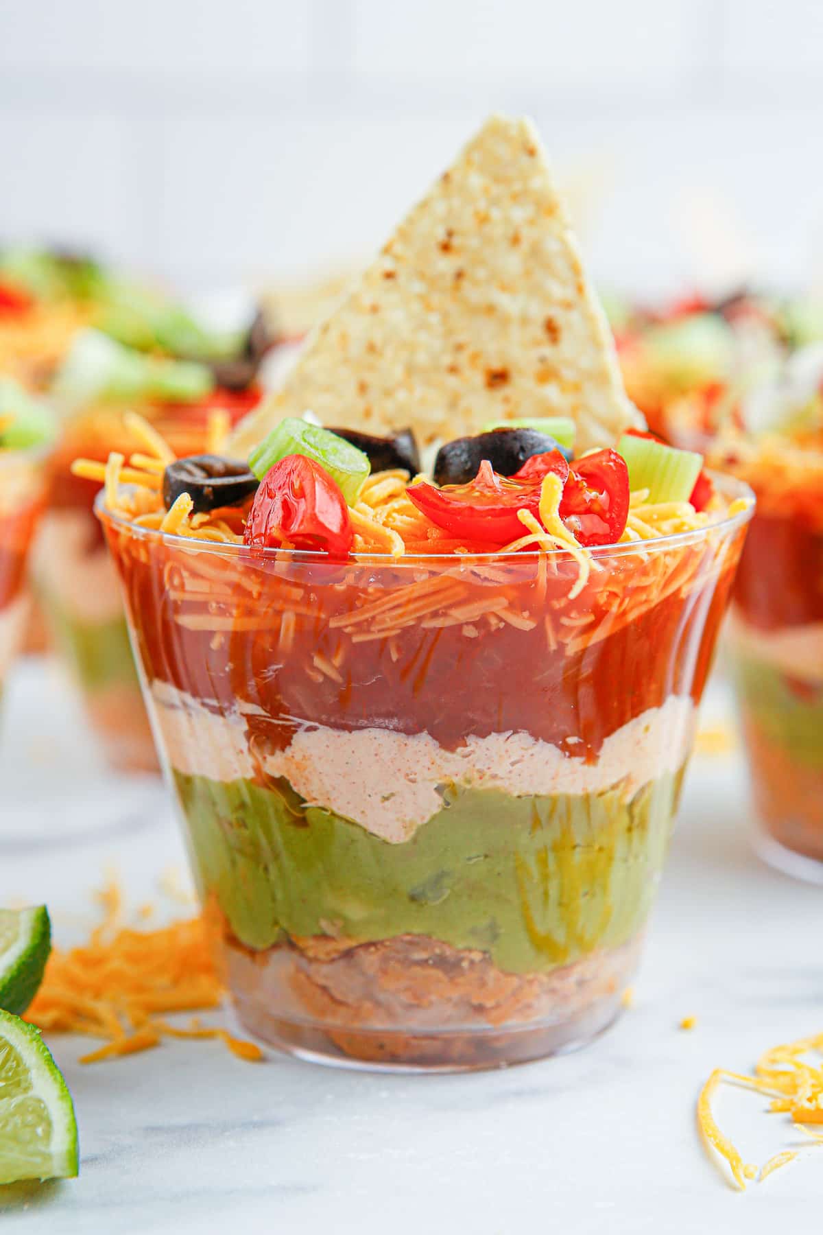 Seven layer dip cup from the side to see the layers through a clear glass with a chip on top and more in the background.