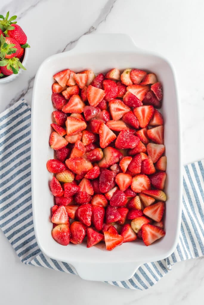 Sliced strawberries mixed with sugar layered in a large baking dish from above.