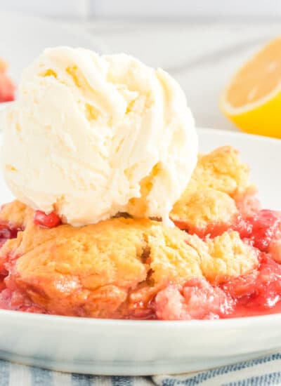 Close up view of the side of a plate with strawberry cobbler and a scoop of vanilla ice cream on top.