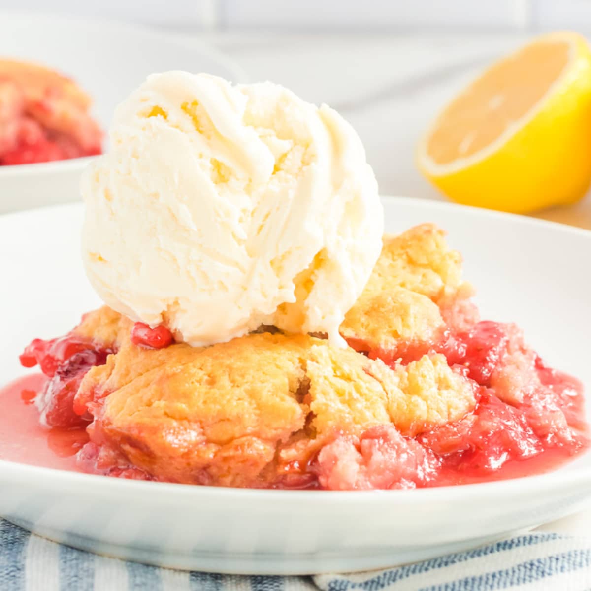 Close up view of the side of a plate with strawberry cobbler and a scoop of vanilla ice cream on top.