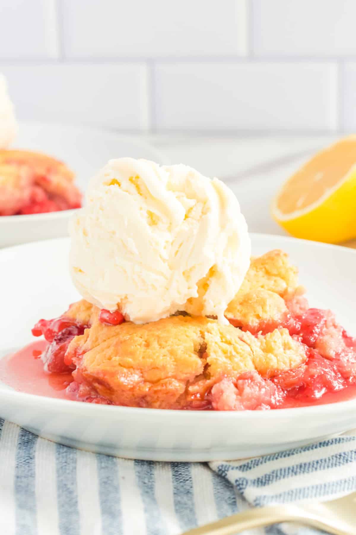 Strawberry cobbler scooped onto a plate with a big scoop of vanilla ice cream from the side.