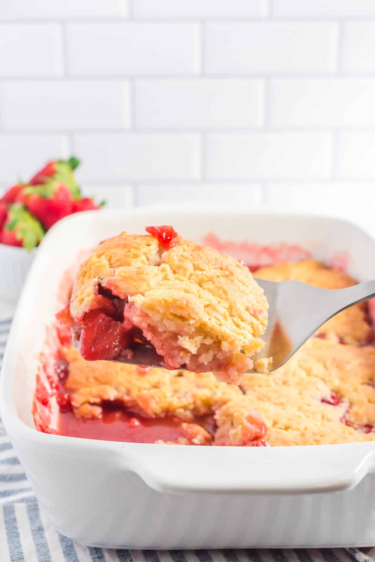 Strawberry cobbler being scooped from a pan from the side.