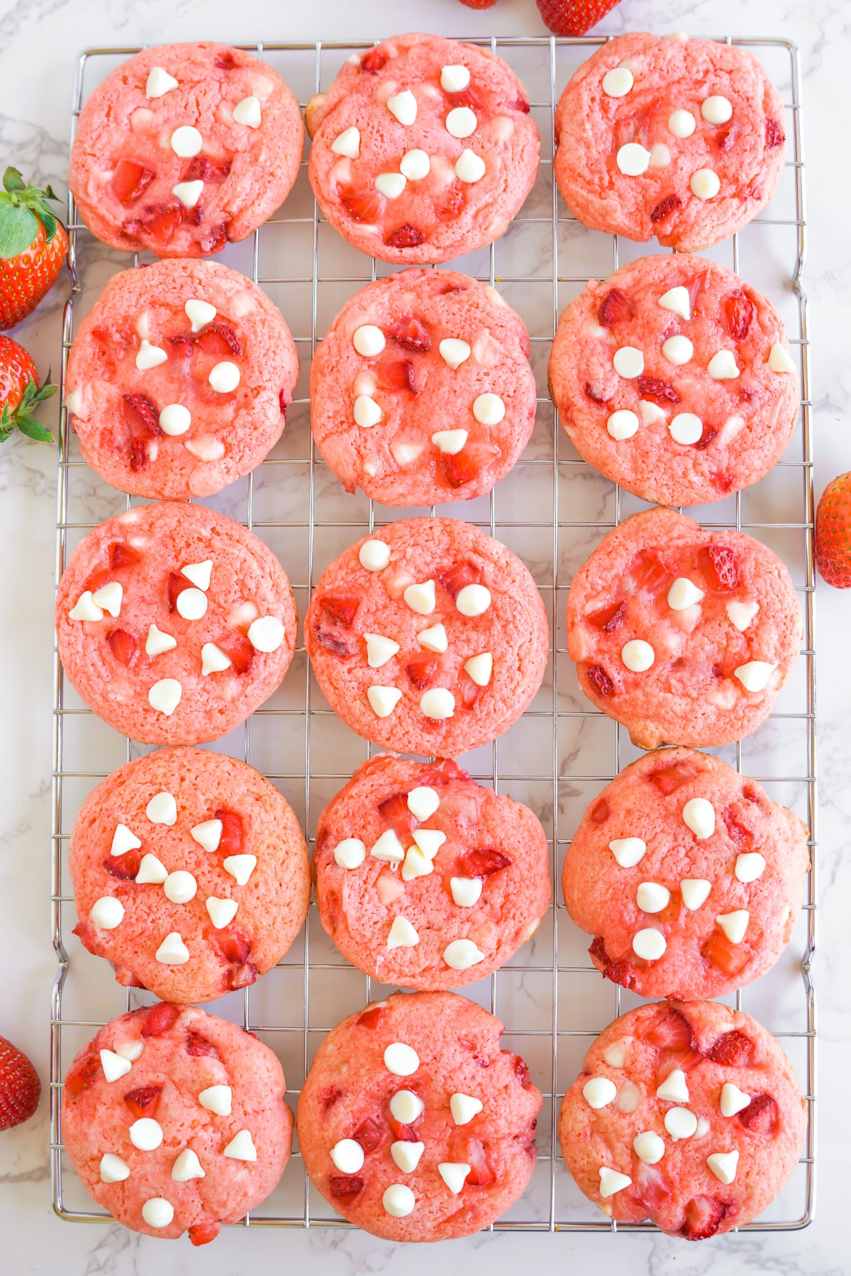 Strawberry cookies topped with white chocolate chips and real strawberry pieces lined up on a wire cooling rack from oeverhead.