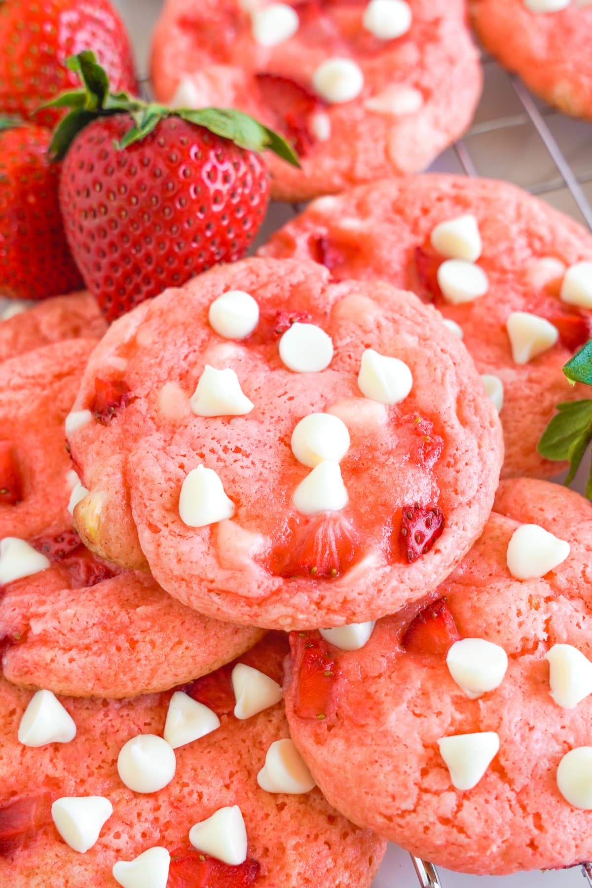 Strawberry white chocolate cookies in a pile from overhead with a fresh strawberry next to the cookies.