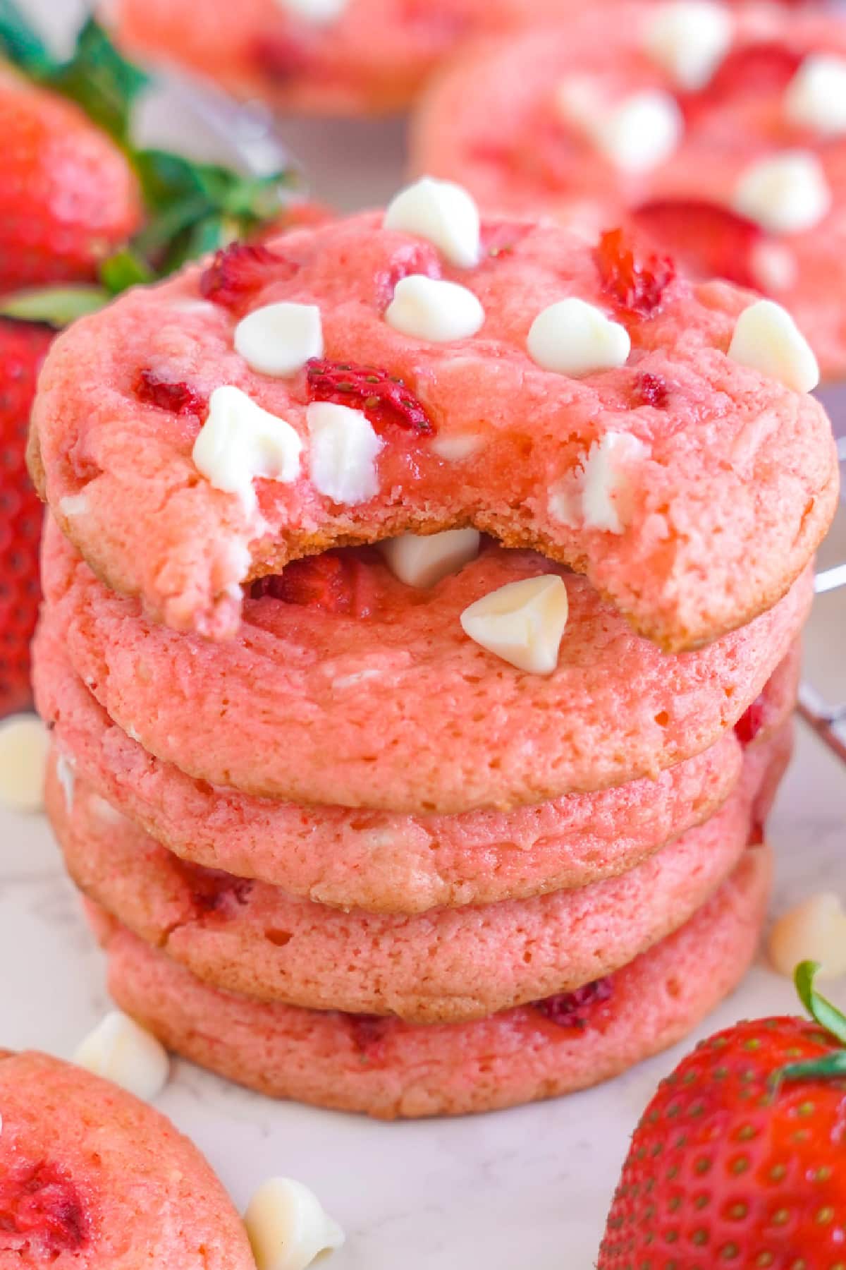 Five pink strawberry white chocolate chip cookies stacked in a tall stack with the top cookie missing a bite.