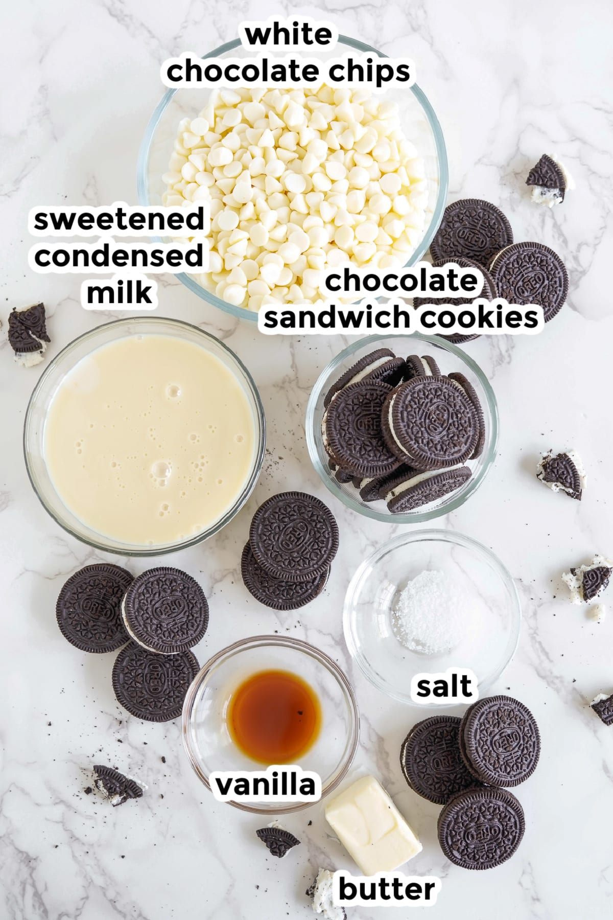 Ingredients for cookies and cream fudge in bowls on a counter from overhead with text labels.