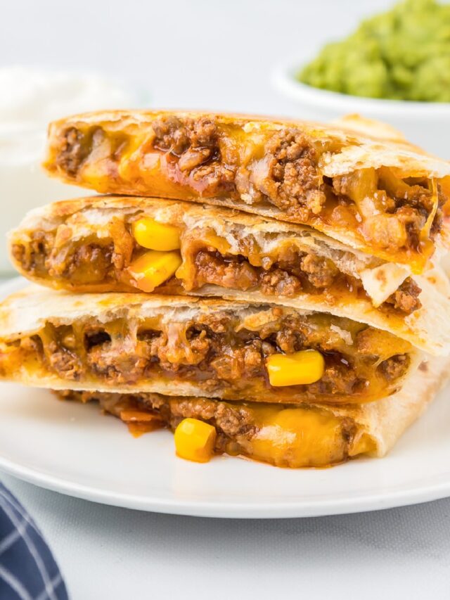 Side view of four quesadillas stacked on a plate from the side to show the beef, corn and cheesy filling.