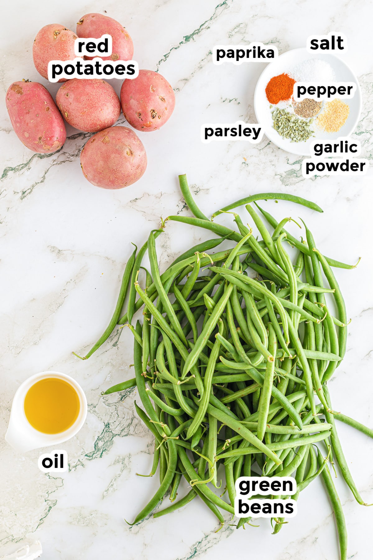 Ingredients for roasted potatoes and green beans on a counter with some in bowls. Text labels are overtop of each ingredient.