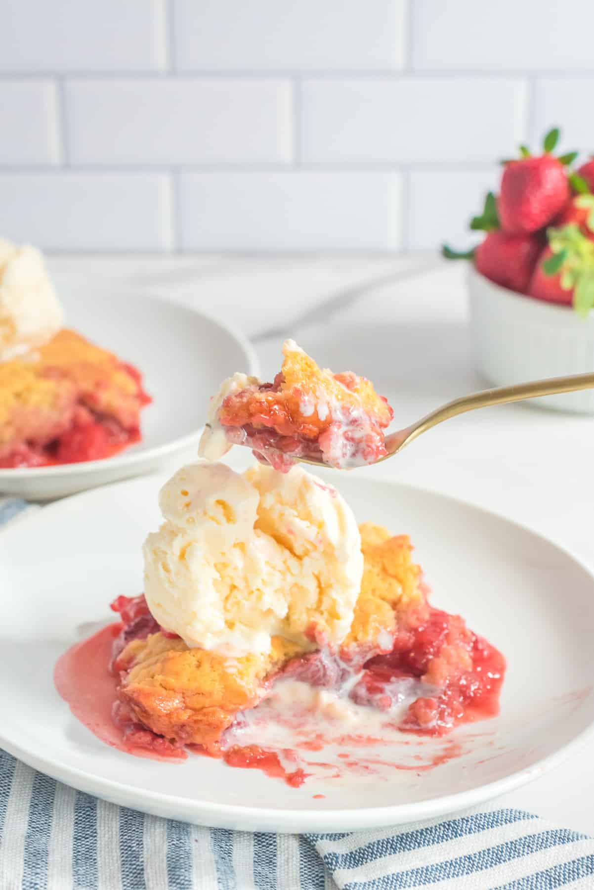 A fork full of strawberry cobbler and ice cream being scooped from a plate on a counter from the side.