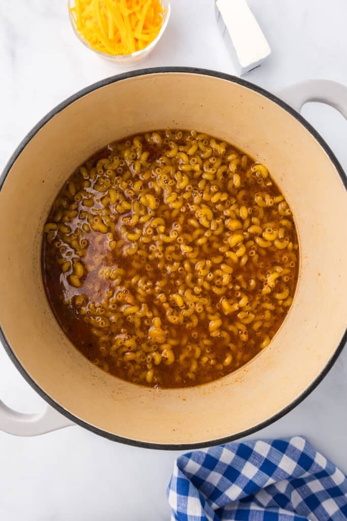Uncooked macaroni in a tomato broth in a large pot from overhead.