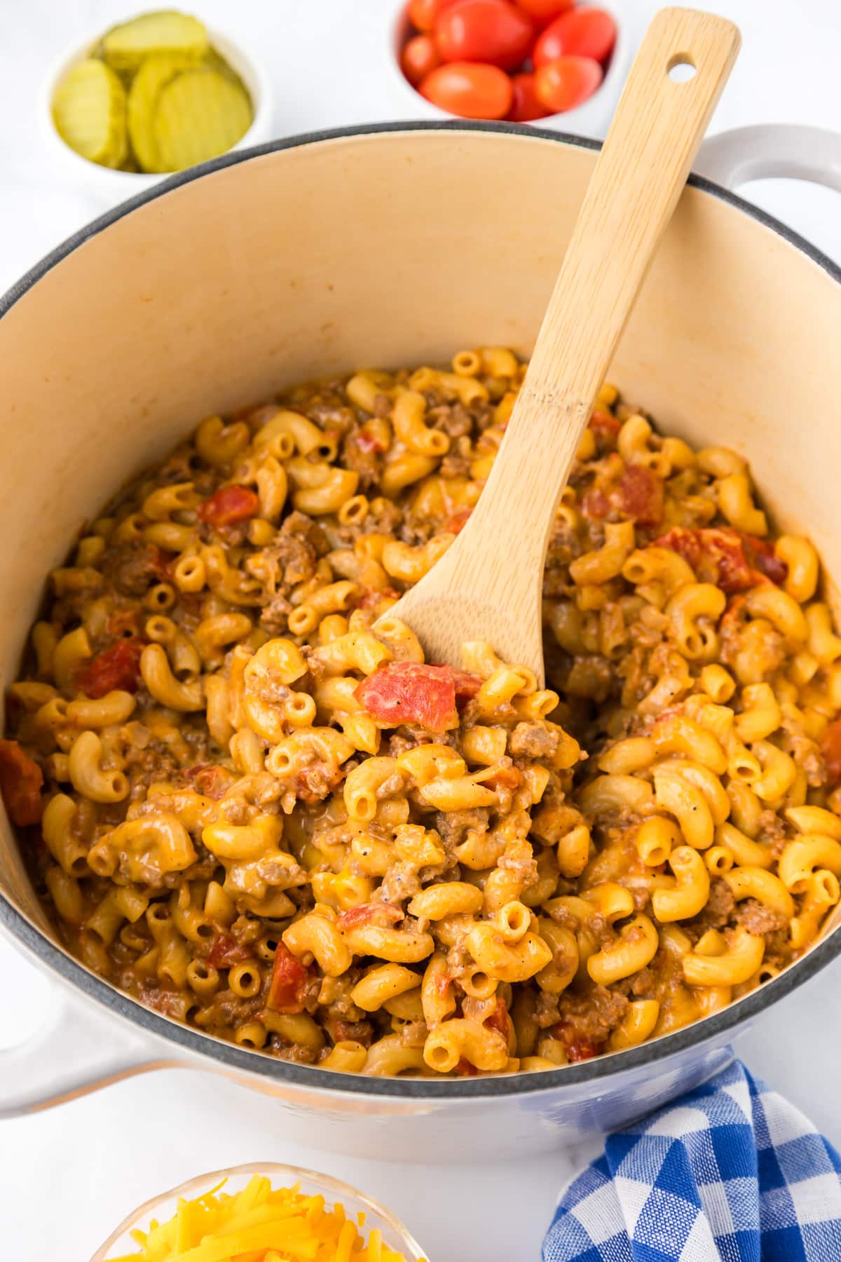 Cheeseburger macaroni finished in a large pot being mixed with a wooden spoon.