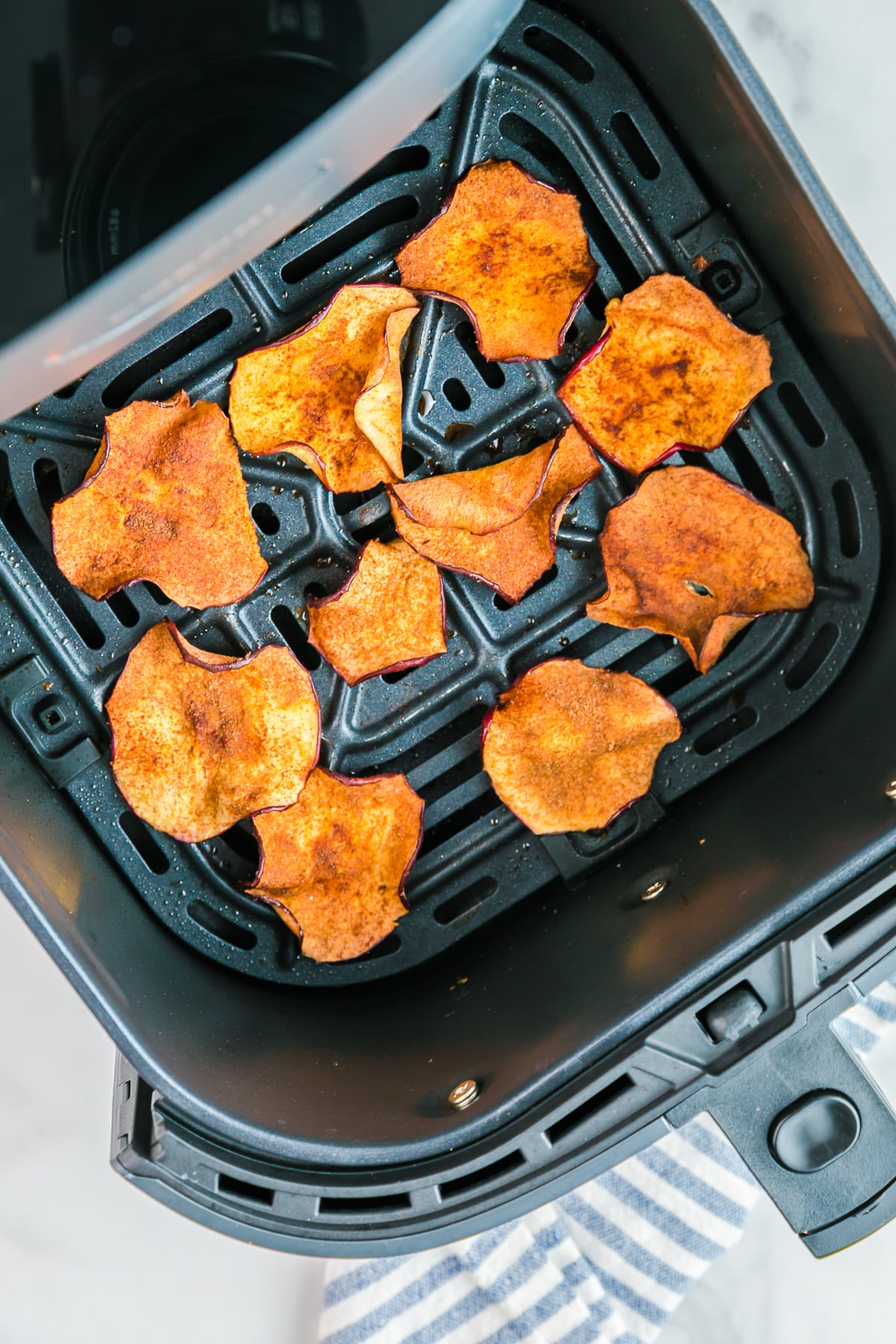 Cooked apple chips in the bottom of an air fryer basket from above.