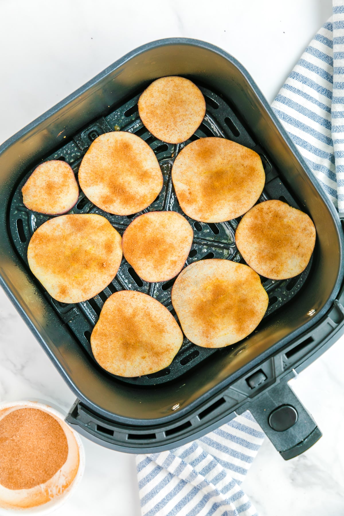 Thin apple slices covered in cinnamon sugar from overhead in an air fryer basket.