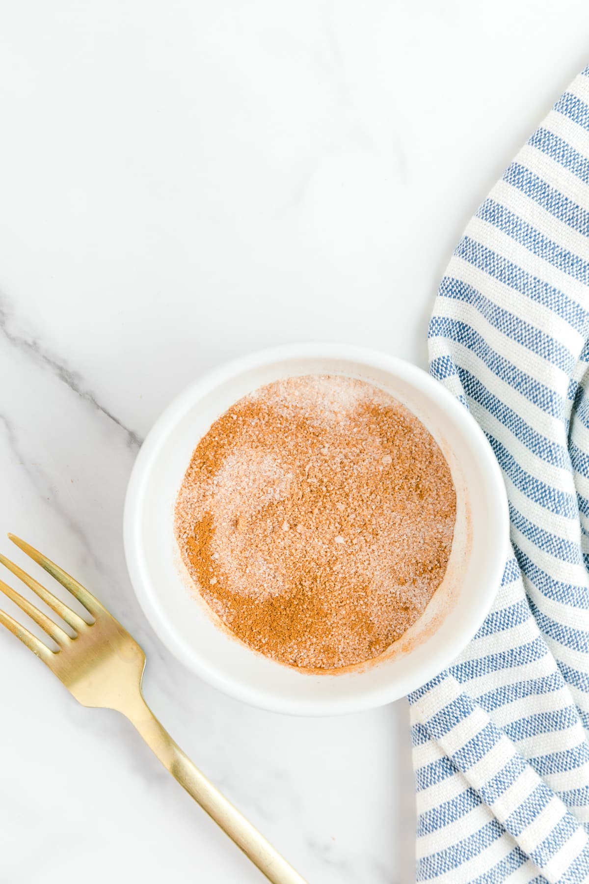 Cinnamon sugar mixed in a small bowl from above with a fork o the counter nearby.