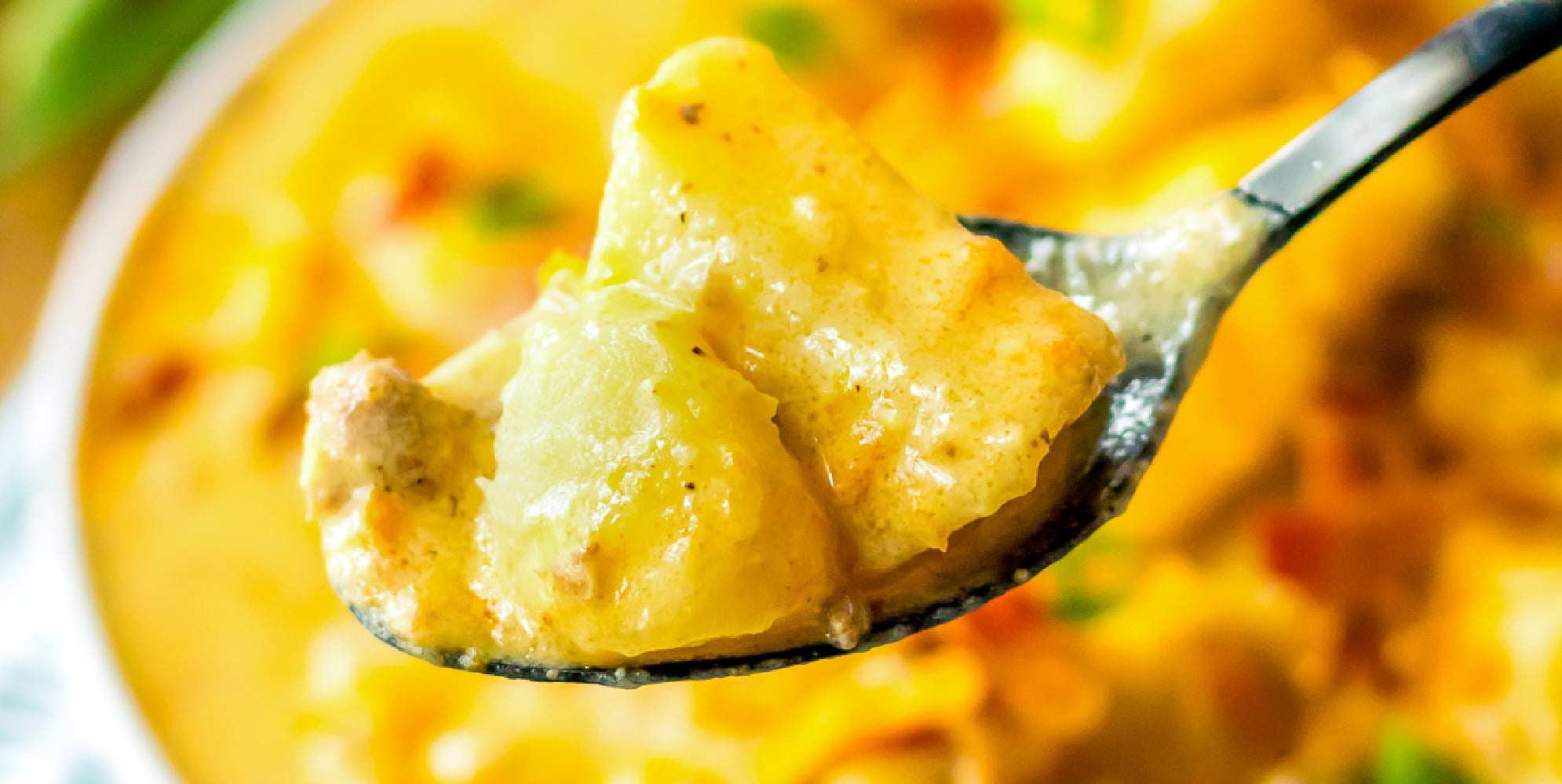 A spoon close up holding a scoop of bacon cheeseburger potato soup.