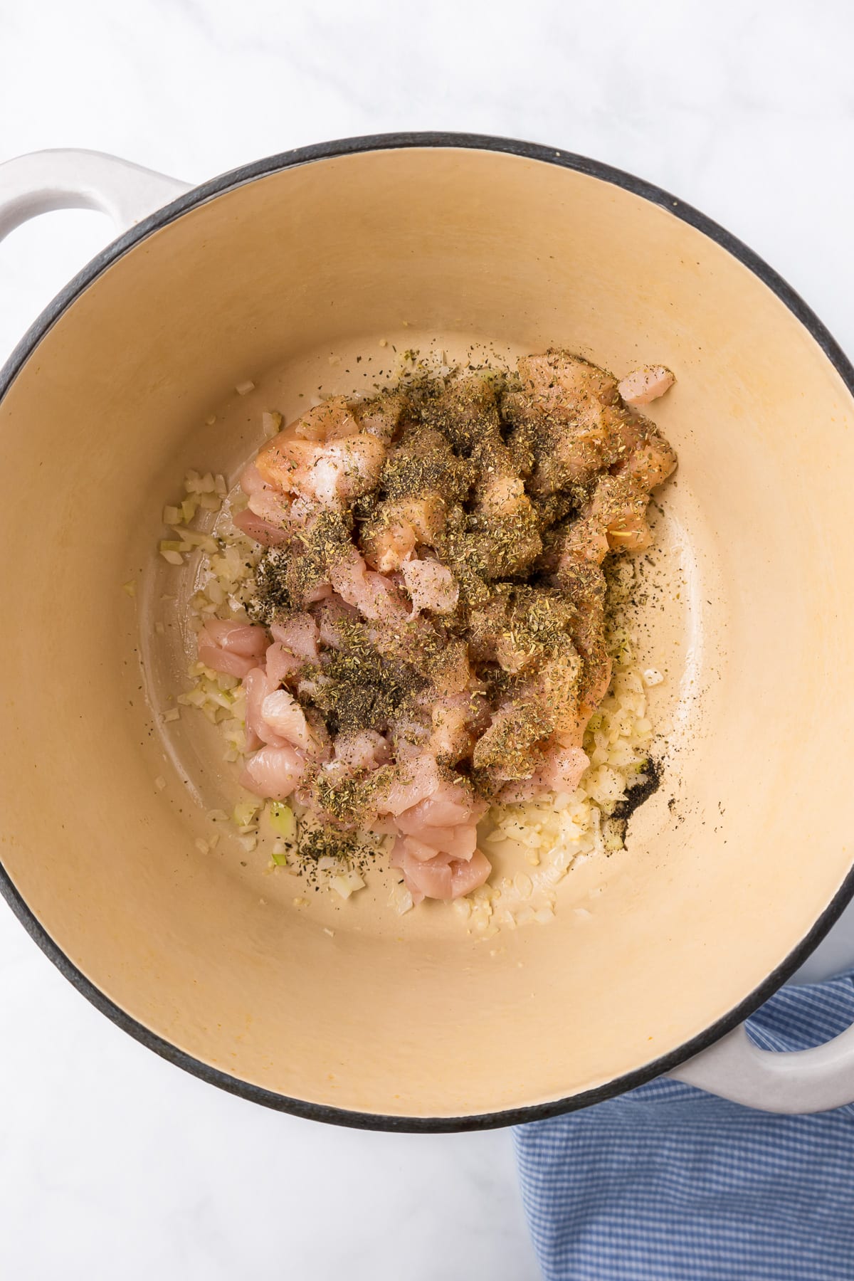 Raw chicken pieces covered in seasoning in a pot being cooked.