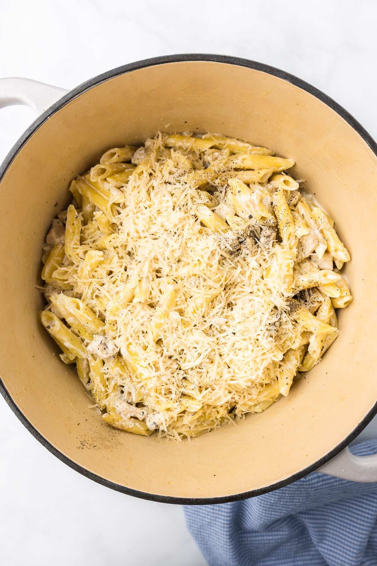 Mixing alfredo sauce and cheese into penne pasta in a pot from above.