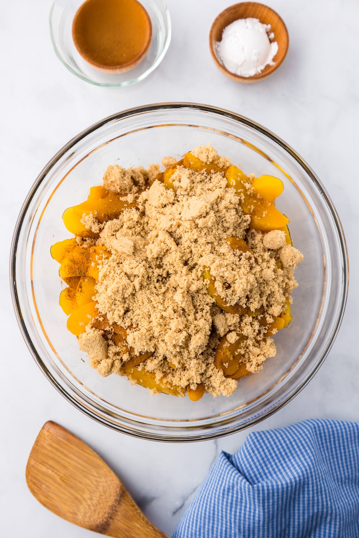 Peaches, brown sugar, cinnamon and other ingredients being mixed together in a large bowl from overhead.