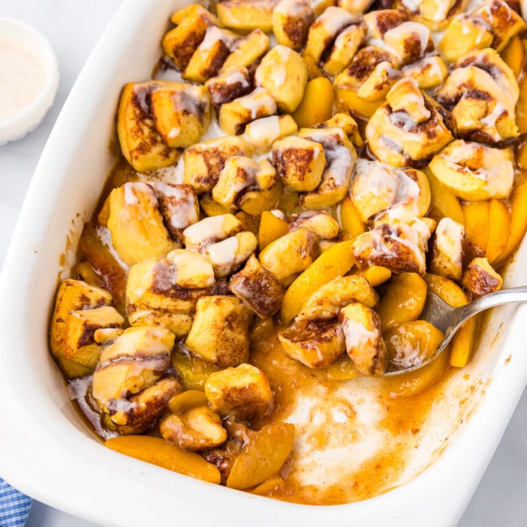 Square view of cinnamon roll peach cobbler in a pan from overhead with a spoon scooping a scoop.