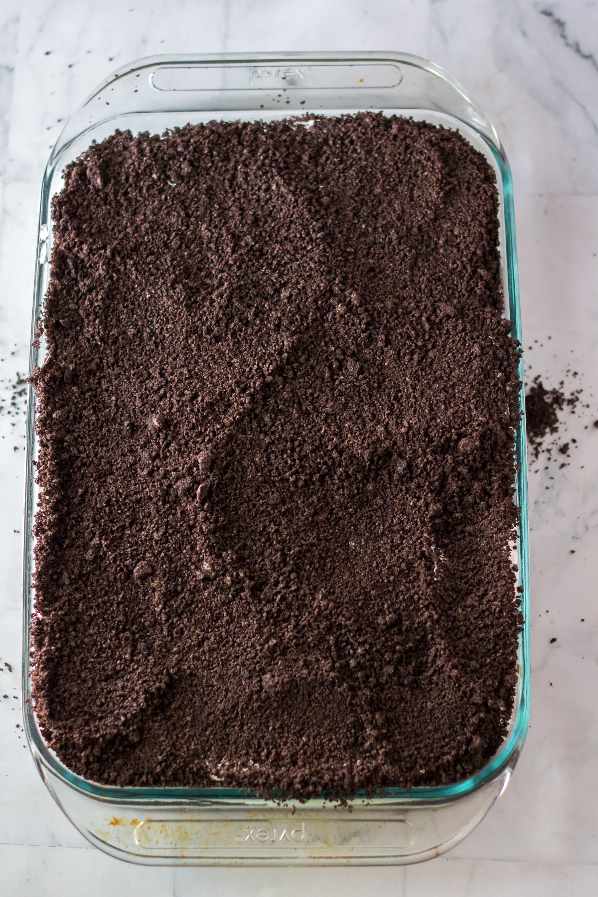 Poke cake in pan covered in chocolate Oreo cookie crumbs.