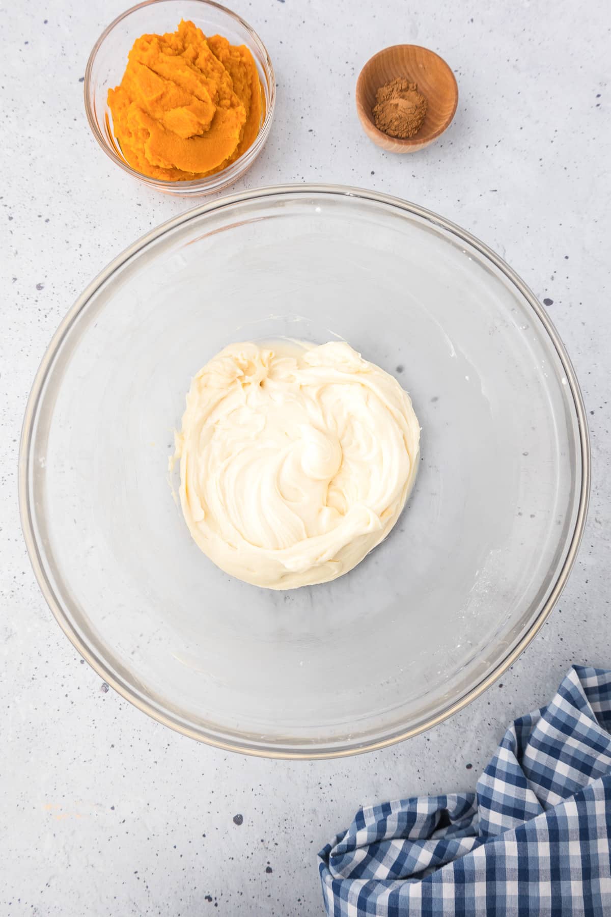 Cream cheese mixture in a bowl with pumpkin and pumpkin pie spice in bowls nearby on the counter from overhead.