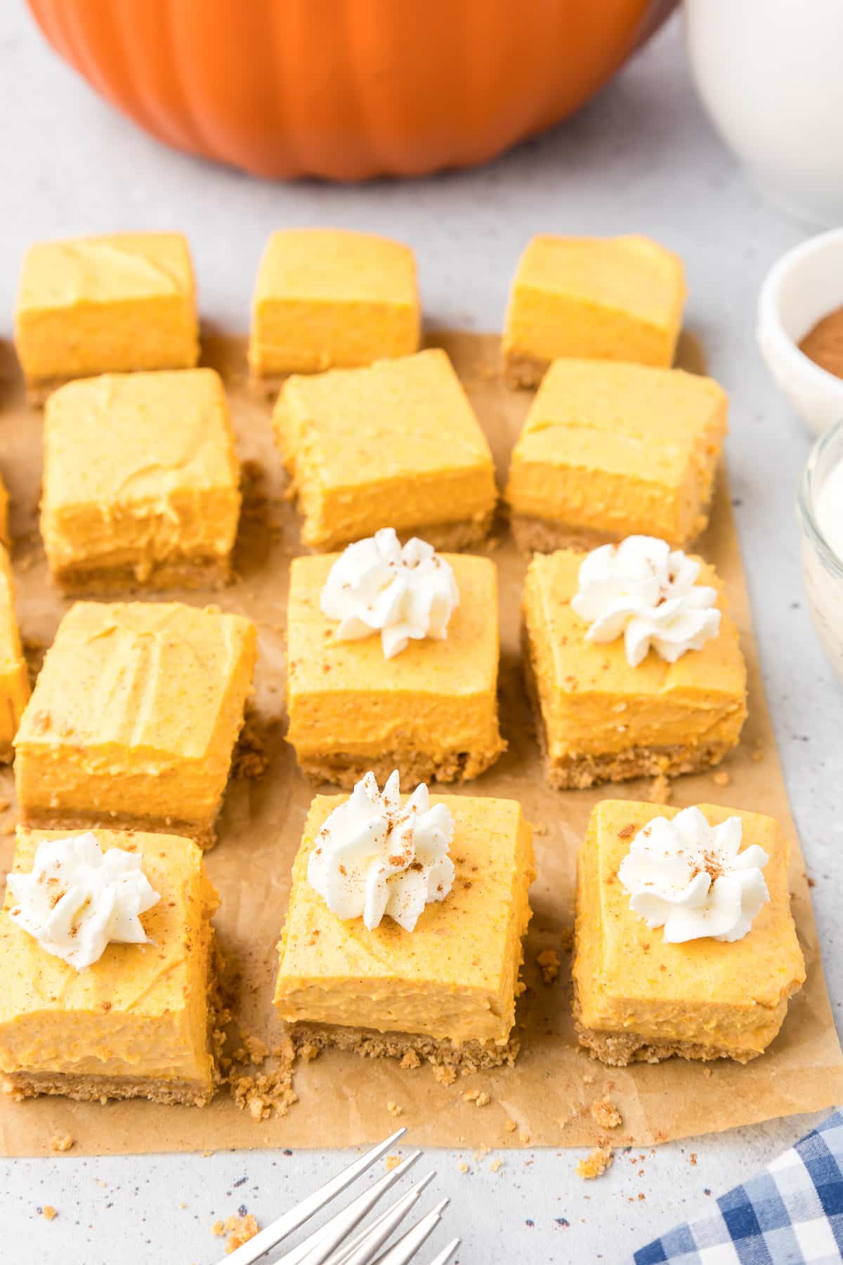 Sliced pumpkin bars from the side on parchment paper with a few bars with whipped cream and pumpkin spice garnish.