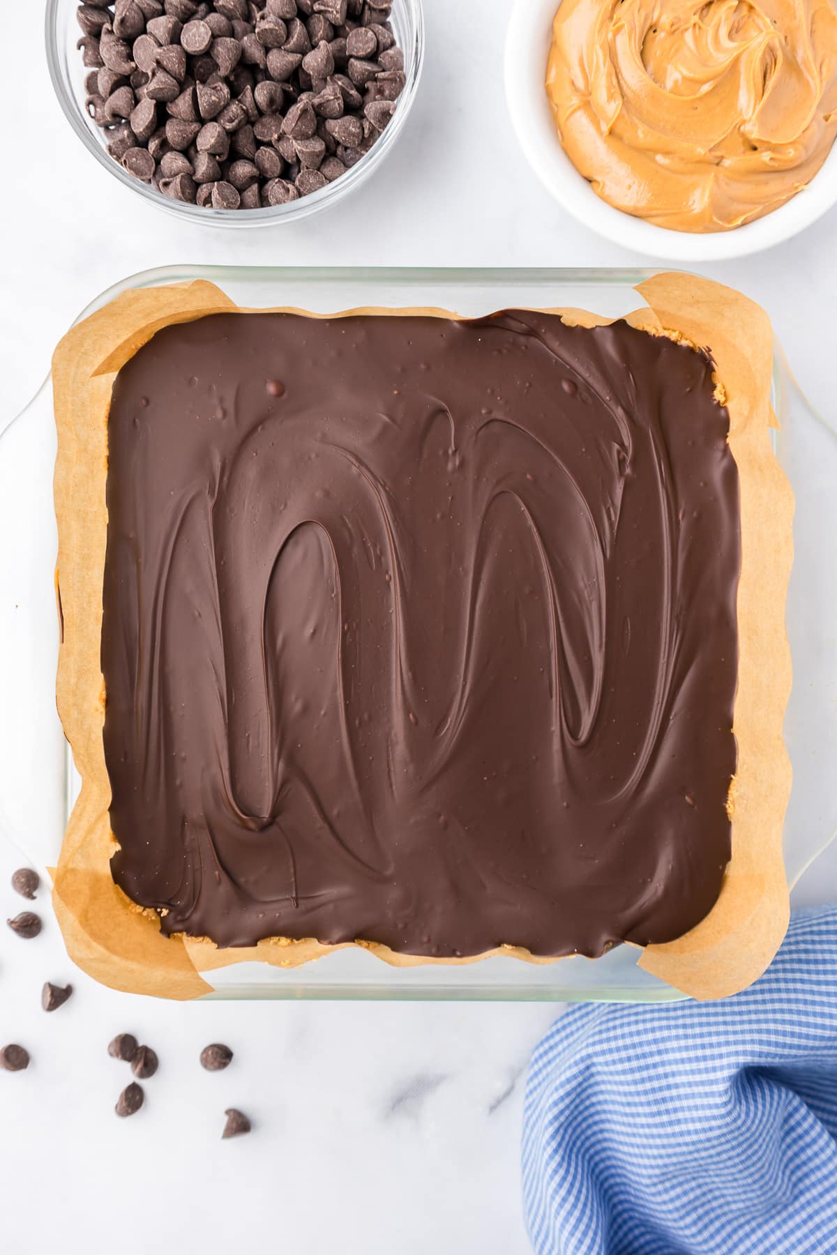 Peanut butter bars topped with chocolate in a square pan from above on a counter.