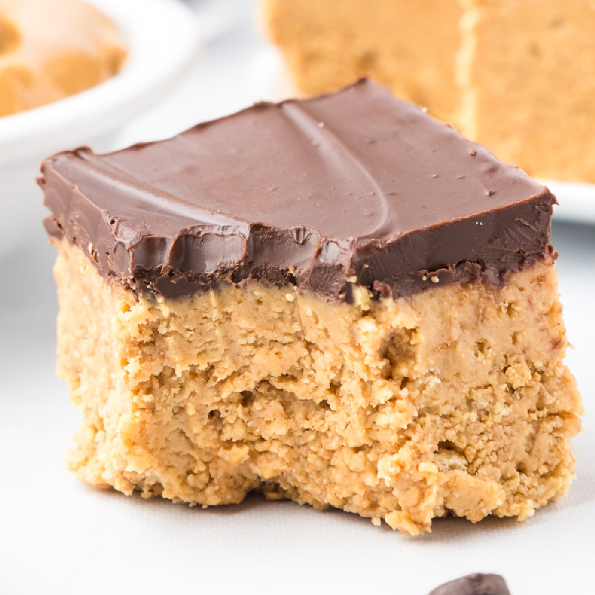 Close up square view of a peanut butter square topped with chocolate missing a bite on a counter.