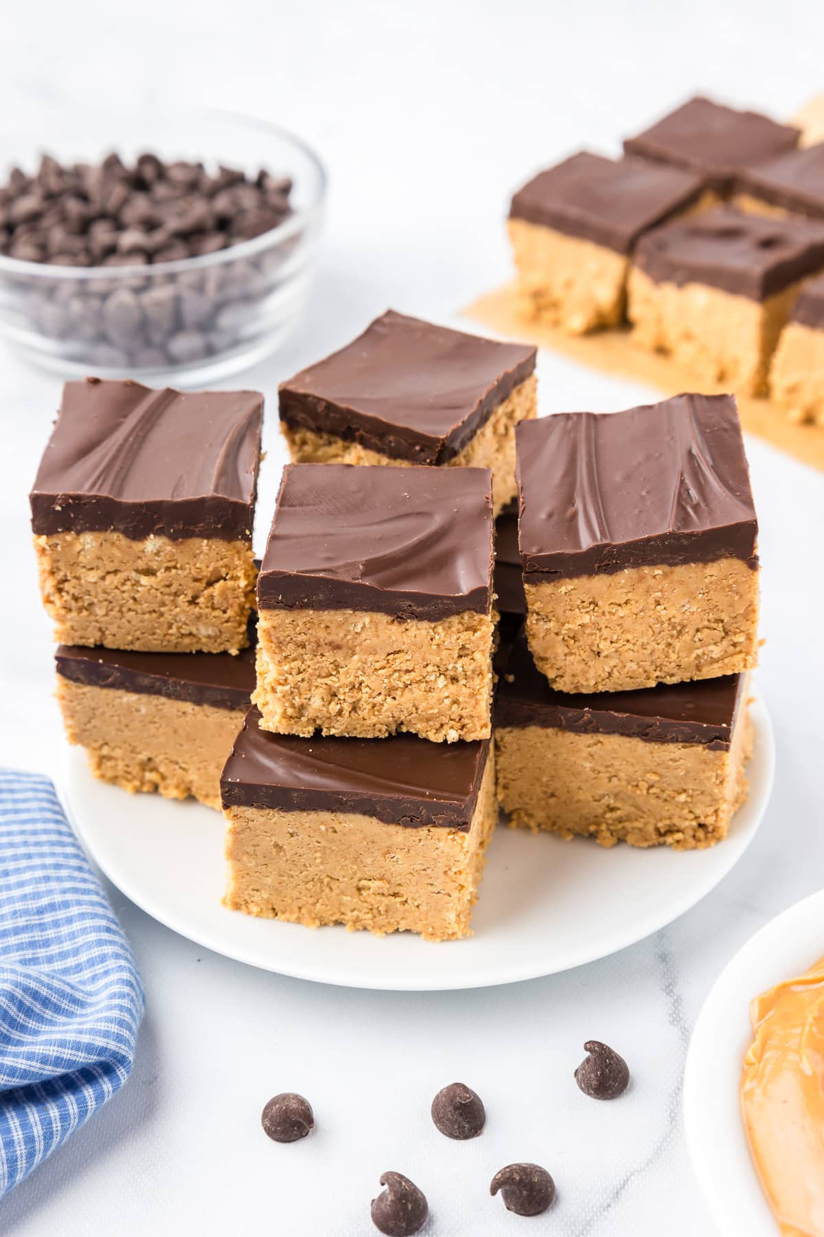 Peanut butter squares topped in chocolate stacked high on a plate.