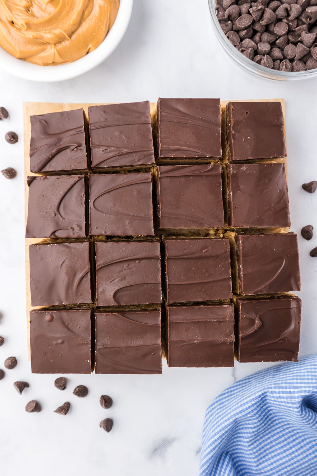 Peanut butter bars topped with chocolate sliced into pieces from above on parchment paper.