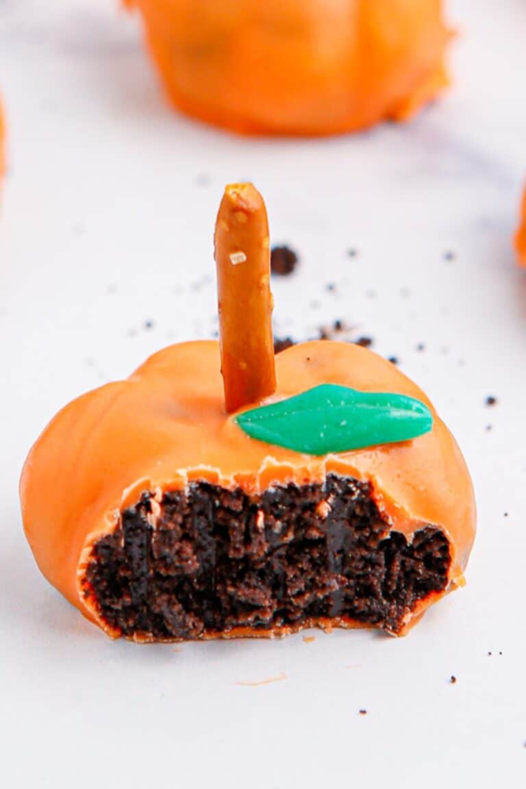 Pumpkin oreo ball missing a bite to see the chocolate inside the pumpkin truffle.