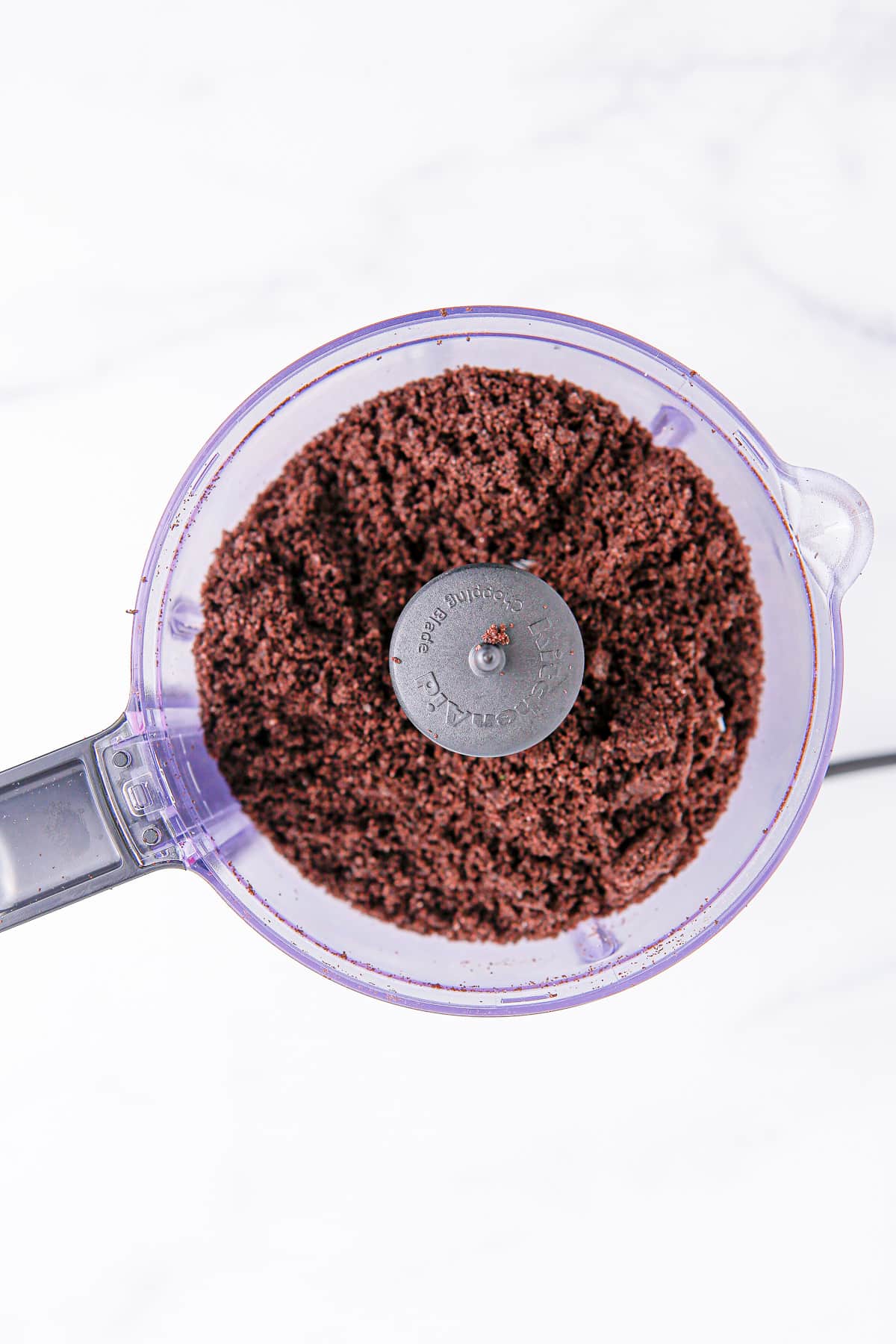 Oreo's turned into crumbs in a food processor from above on a counter.
