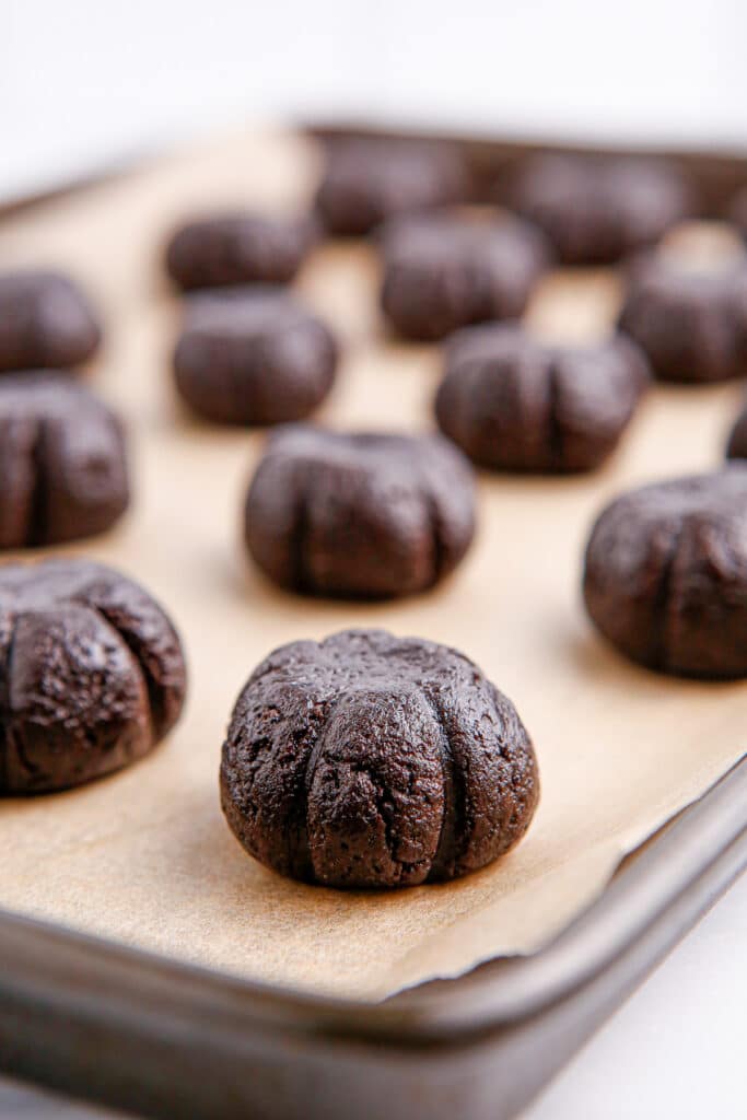 Chocolate Oreo balls after being shaped into a pumpkin shape on a cookie sheet from a side angle.