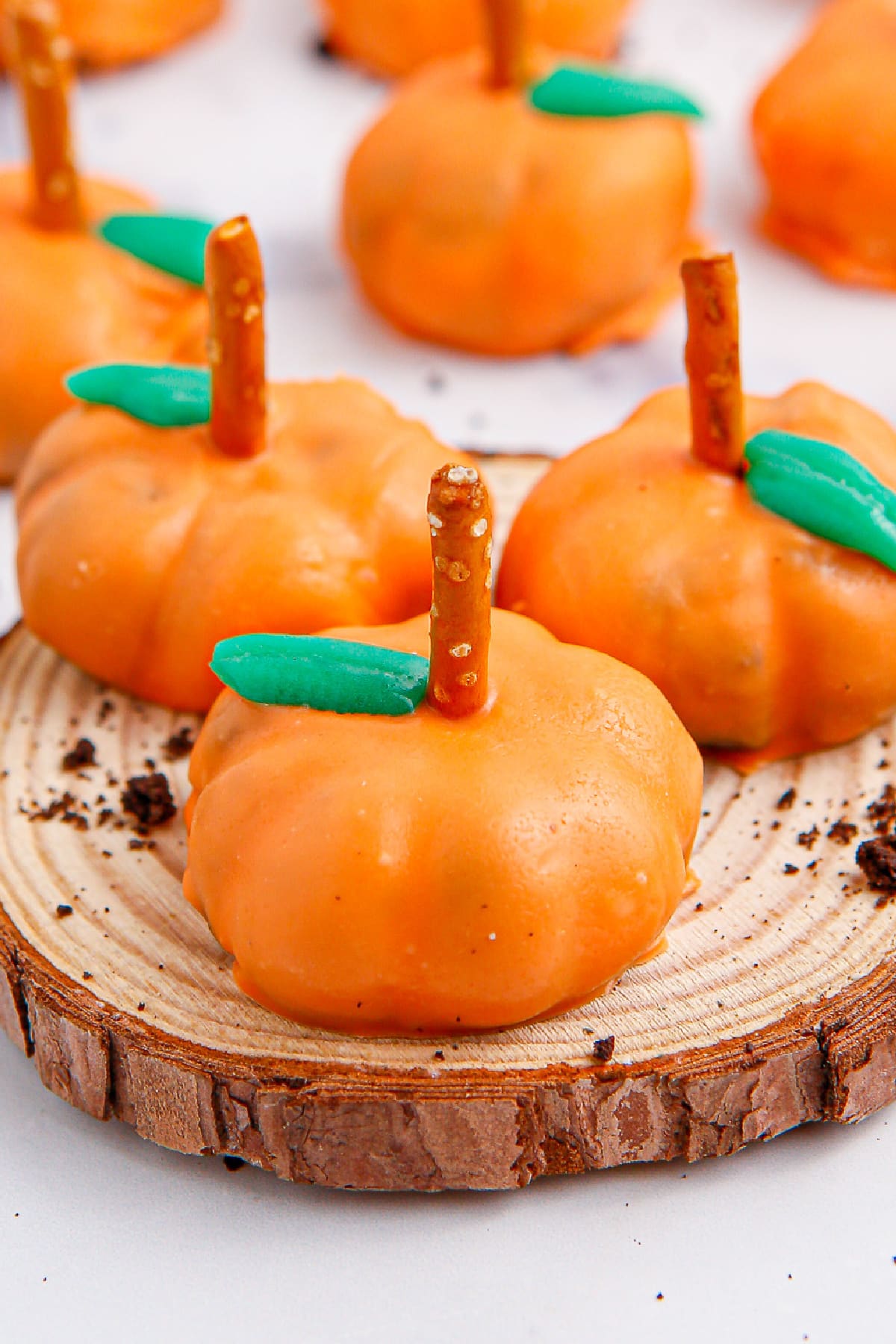 Three oreo ball truffles decorated like pumpkins on a plater with more in the background.