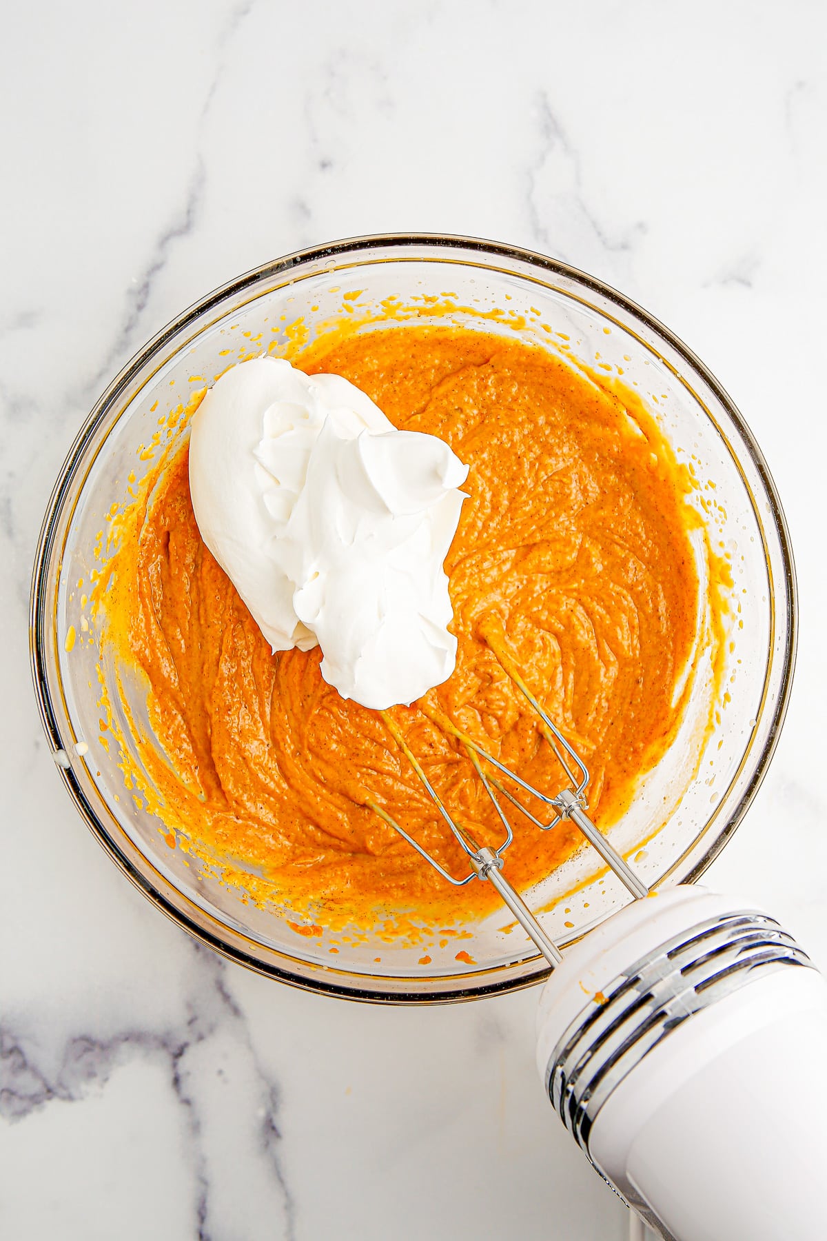 Whipped topping being mixed with an electric mixer in a bowl with pumpkin pudding.