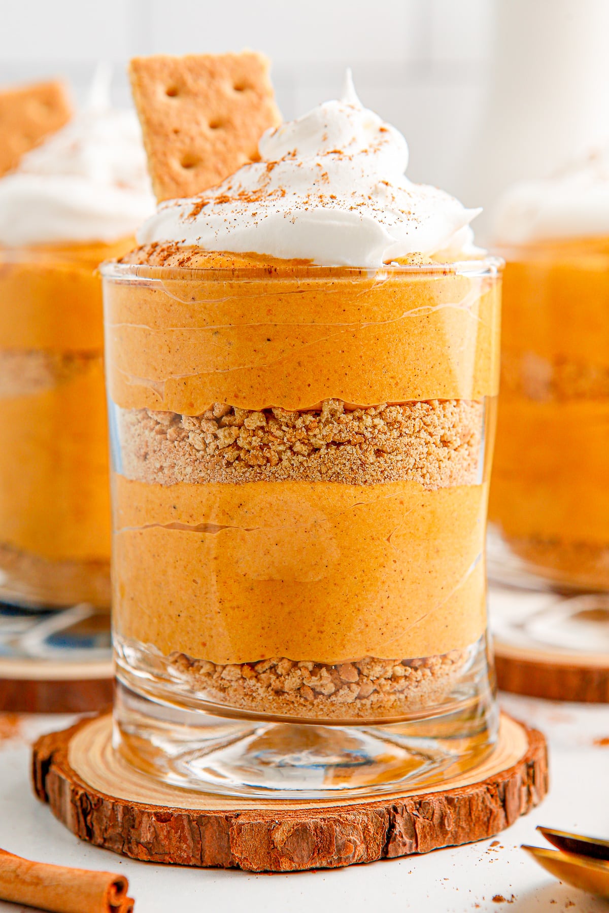 Layered pumpkin pie pudding parfait in a glass topped with whipped cream and a graham cracker.