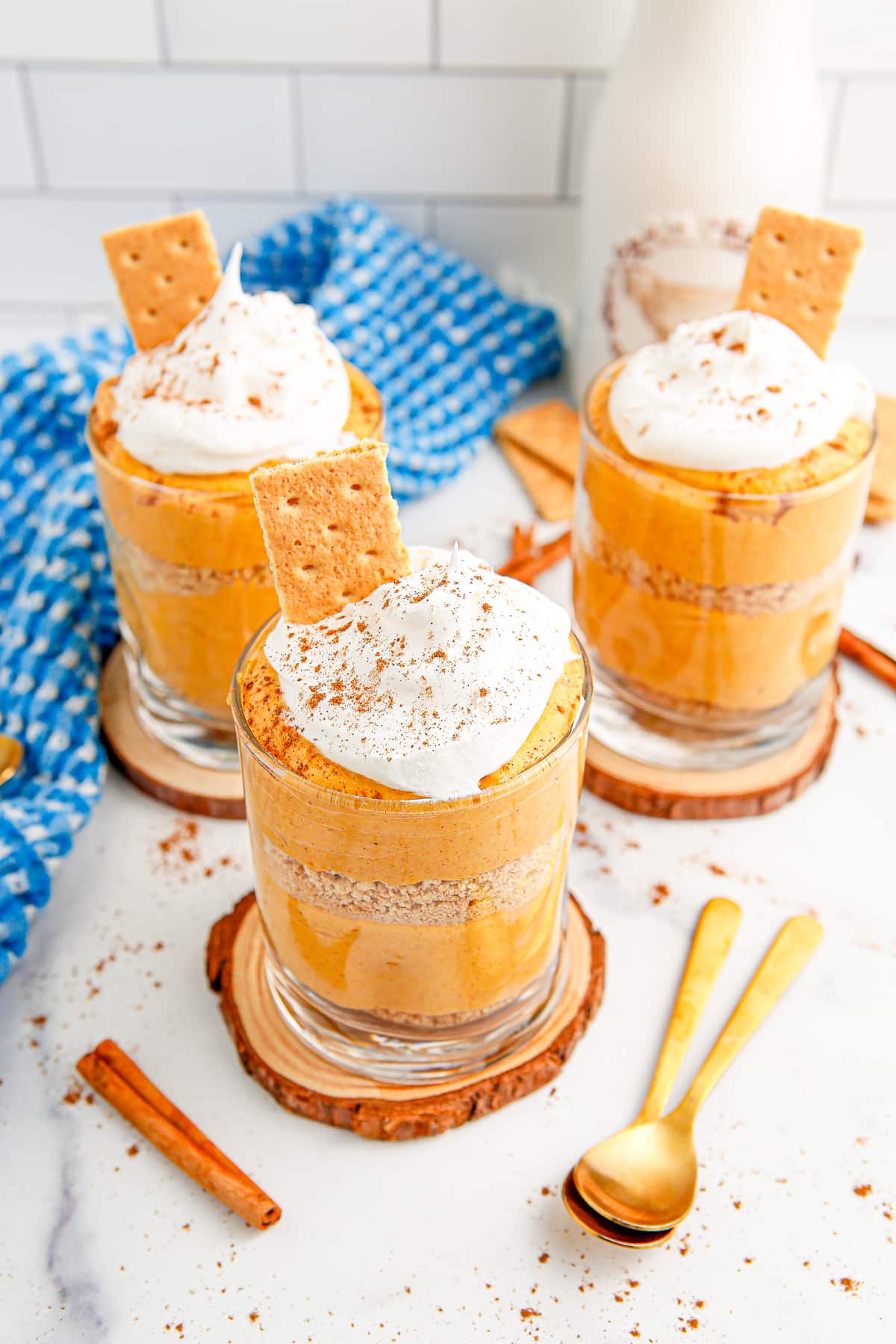 Three Pumpkin pie puddings layered with graham crackers in a glass with whipped cream and cinnamon on top in a kitchen.