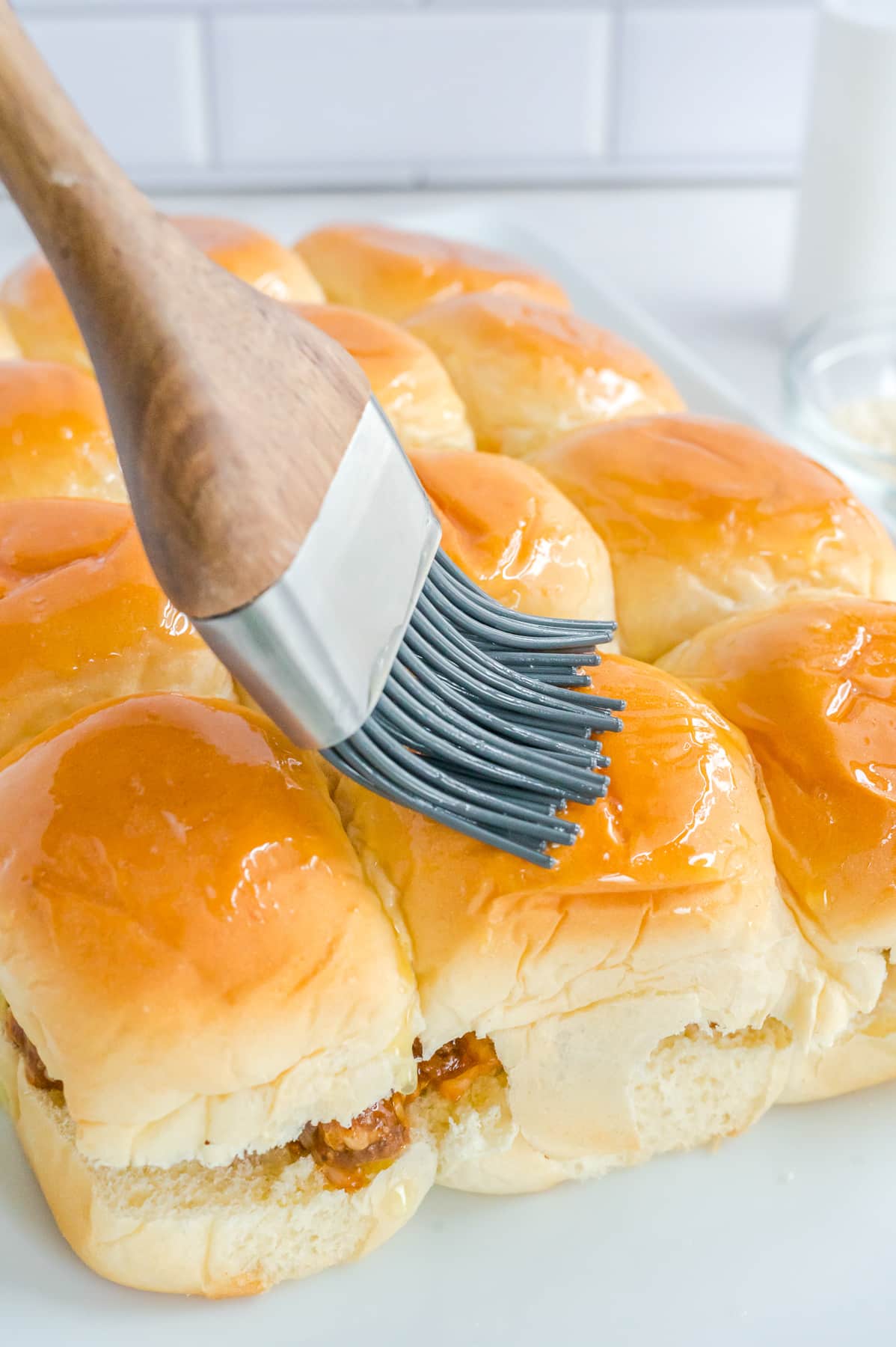 A silicone brush is being used to spread butter on a Hawaiian rolls from the side.
