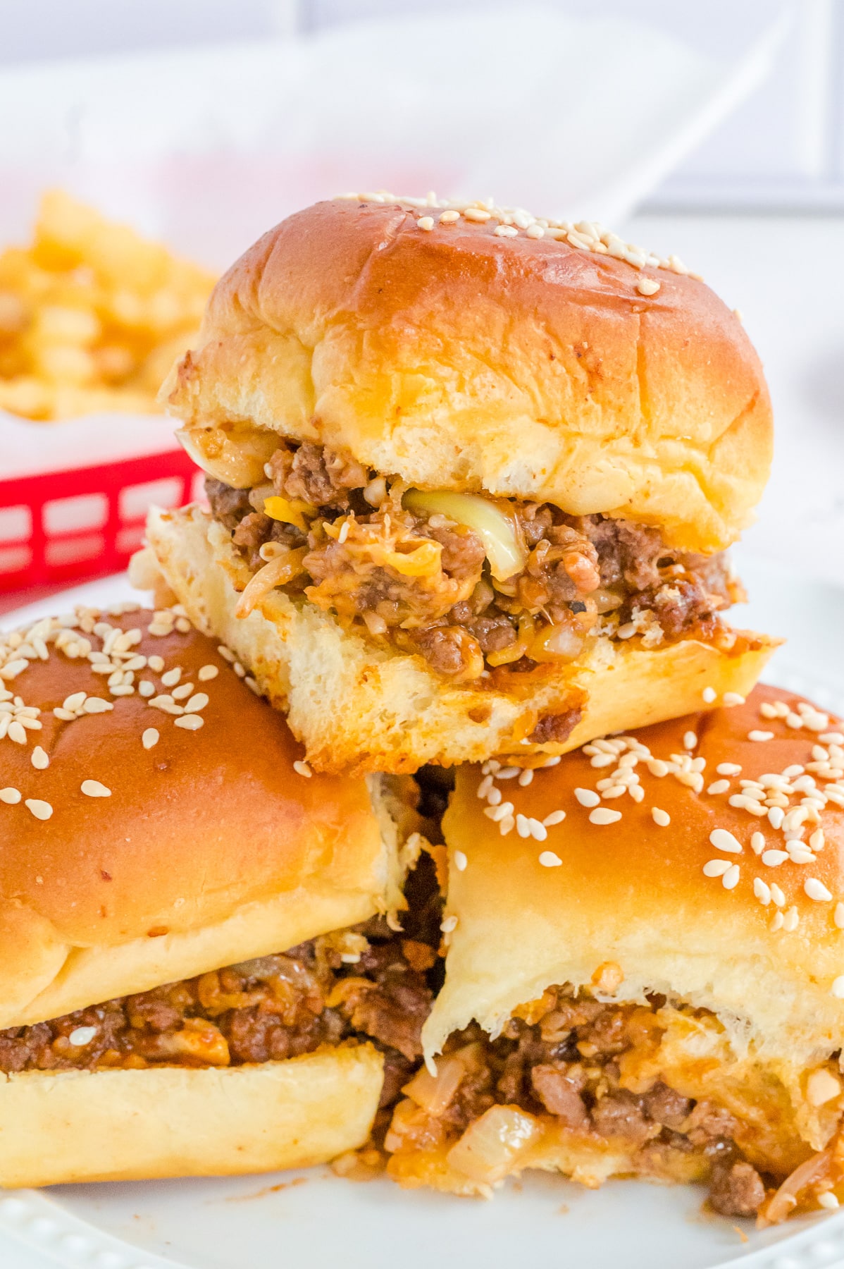 Three sloppy joe sliders stacked on a plate close up from the side with fries in the background.