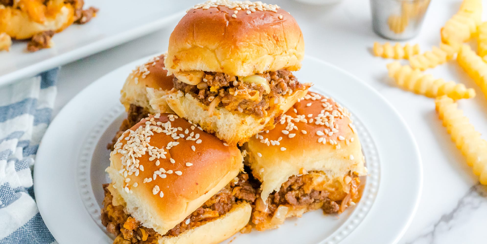 A plate with a stack of sloppy joe sliders on it with a wide view.