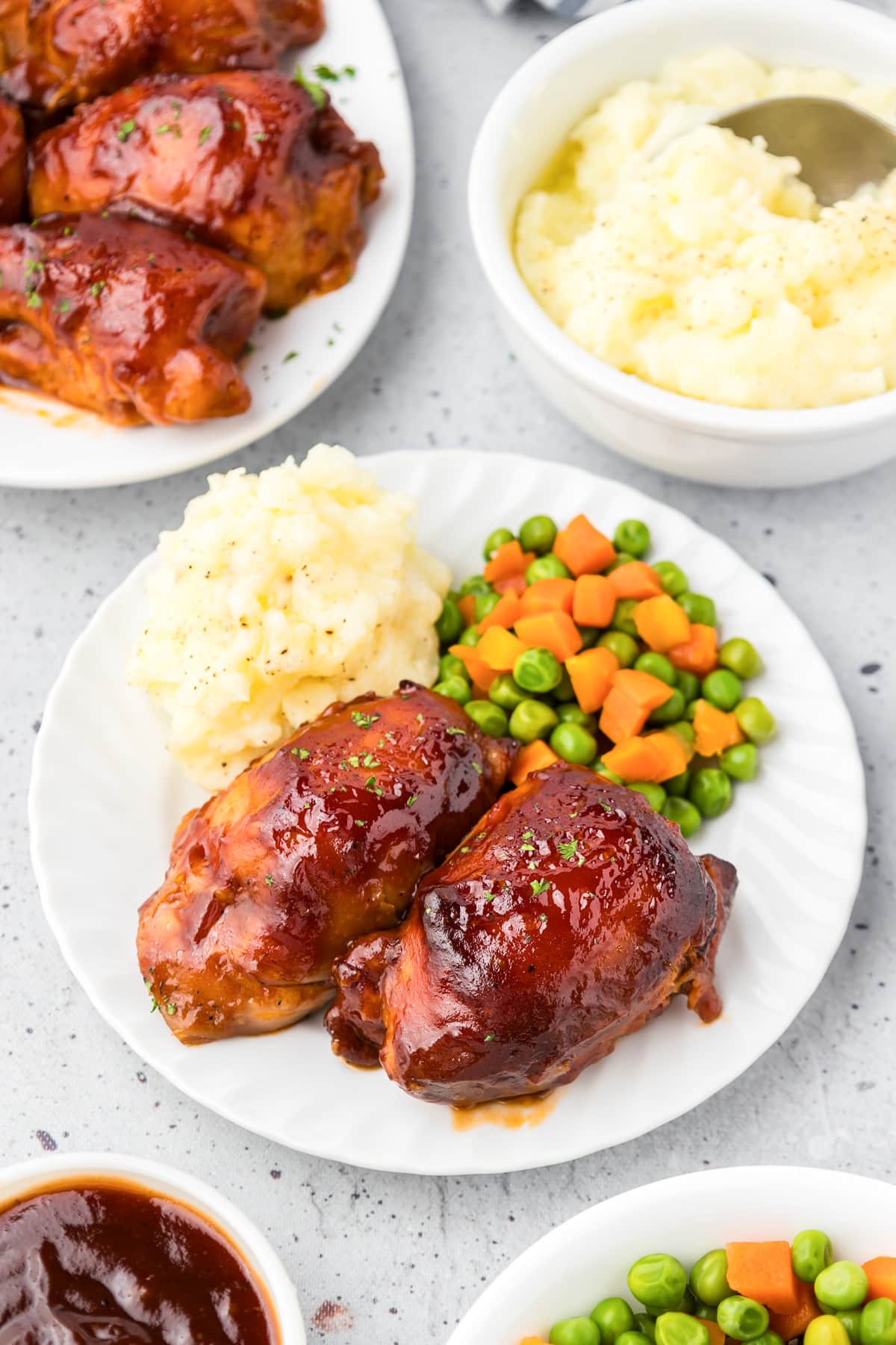 Boneless bbq chicken thighs on a plate with vegetables with other serving dishes full of food nearby on the table.