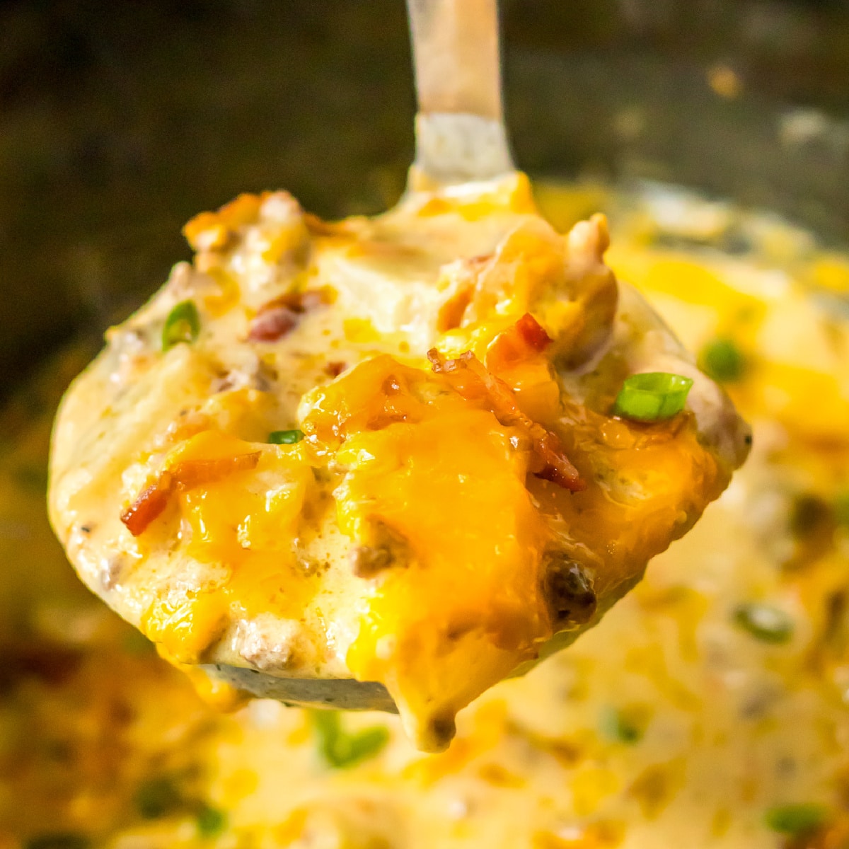 A square view of a ladler full of cheesy bacon cheeseburger soup in a crock pot.