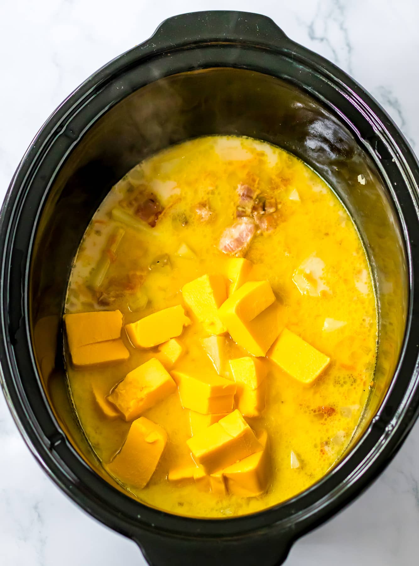 A crock pot filled with mashed potatoes and cubes of cheese.