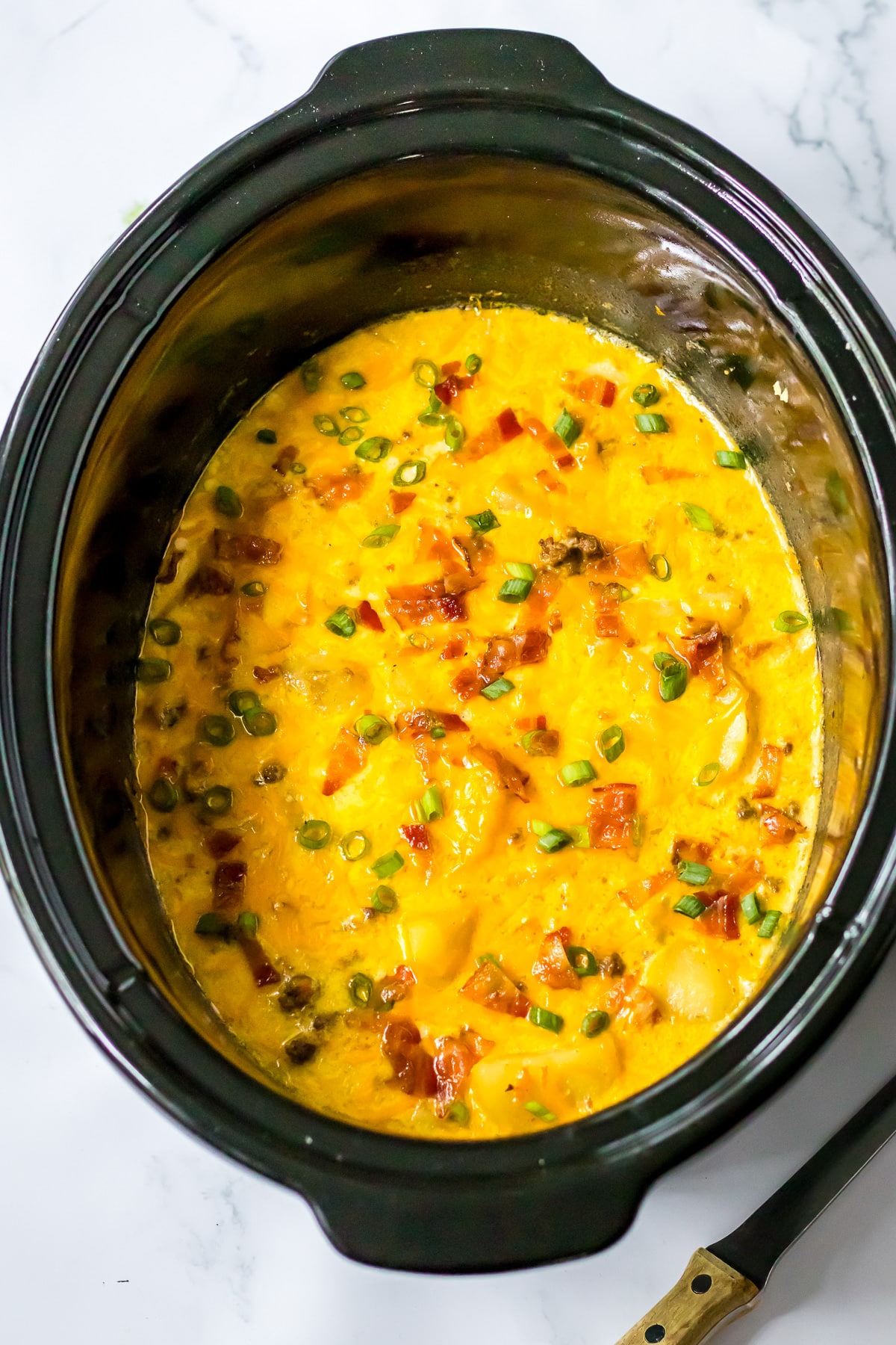 A crock pot filled with cheesy bacon cheeseburger soup from above.