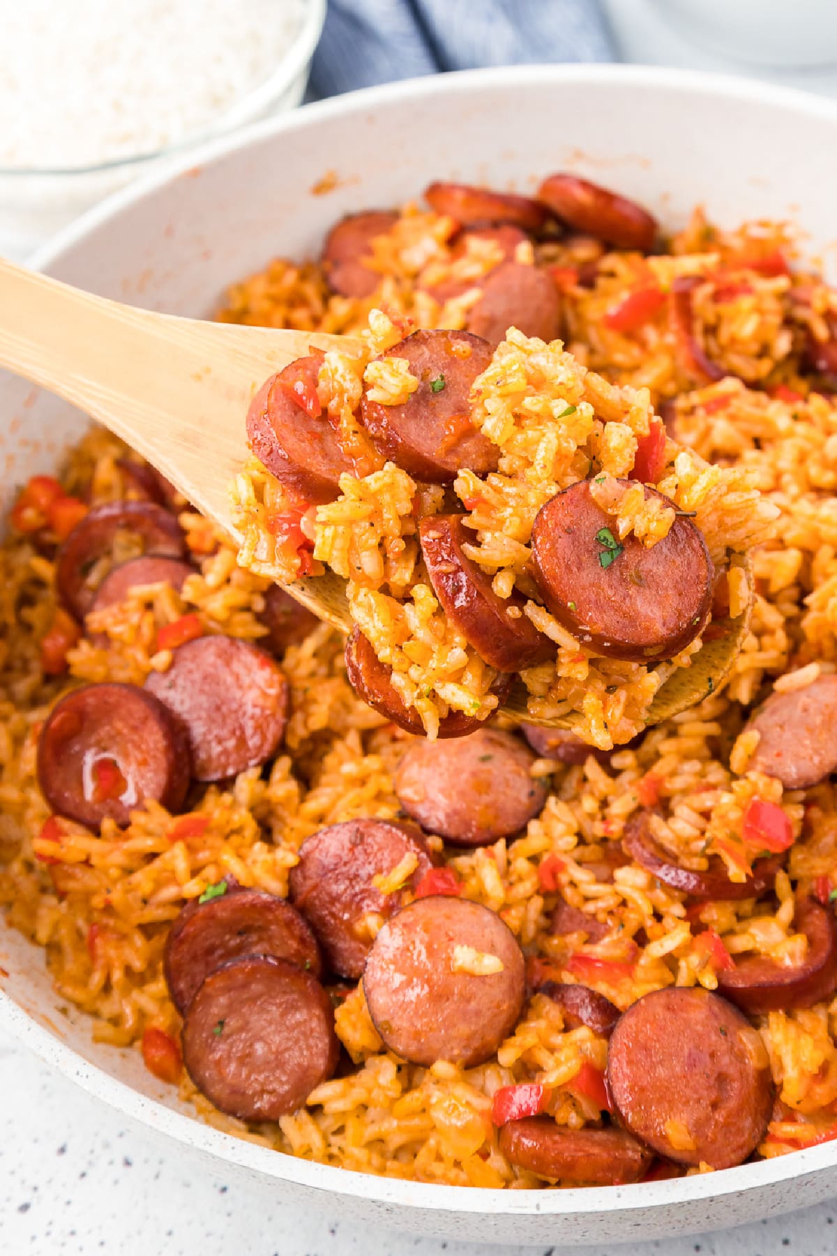 Sausage and red rice in a skillet being scooped with a wooden spoon.