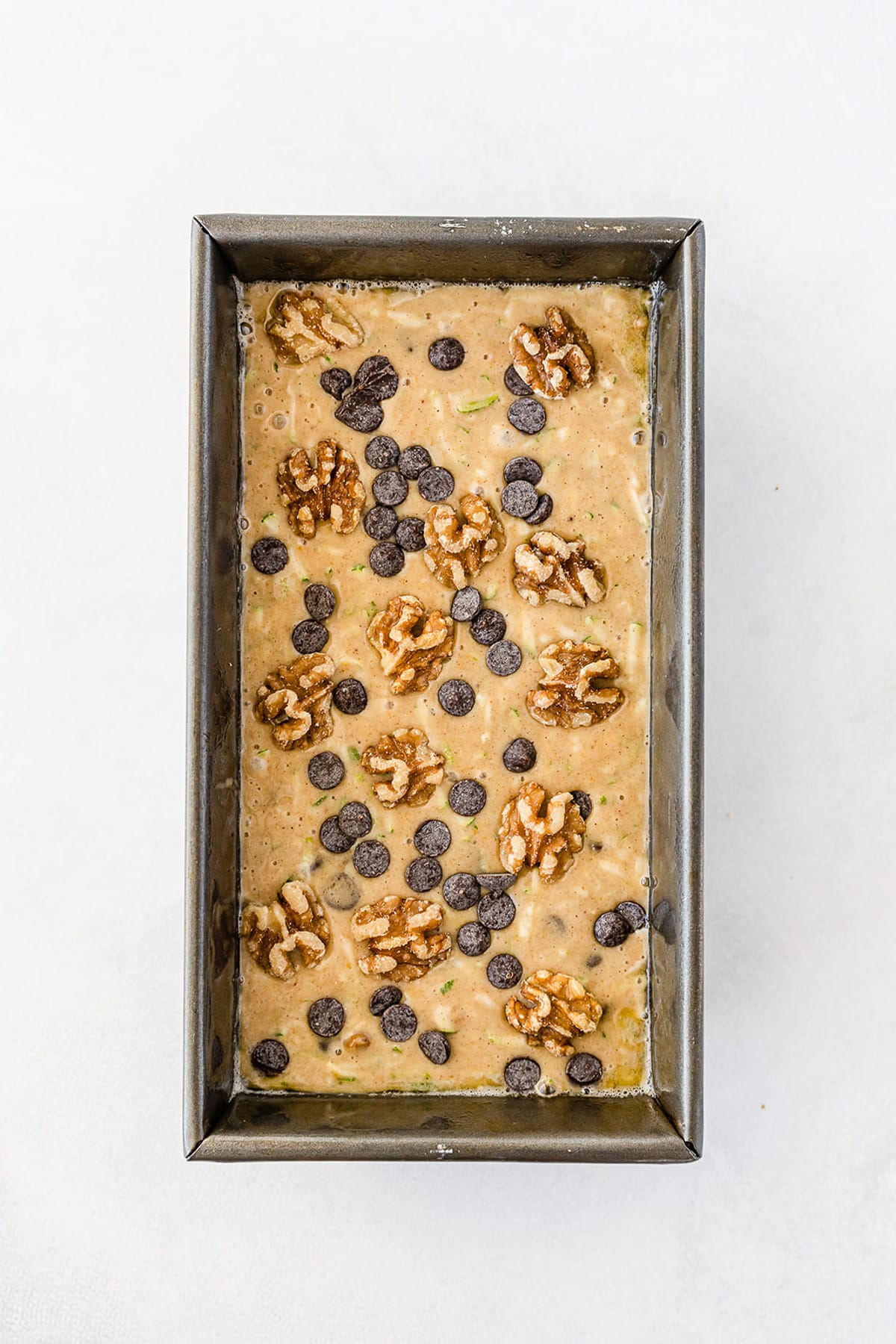 Chocolate chip walnut zucchini bread batter in a bread pan from overhead topped with extra chocolate chips and walnuts.
