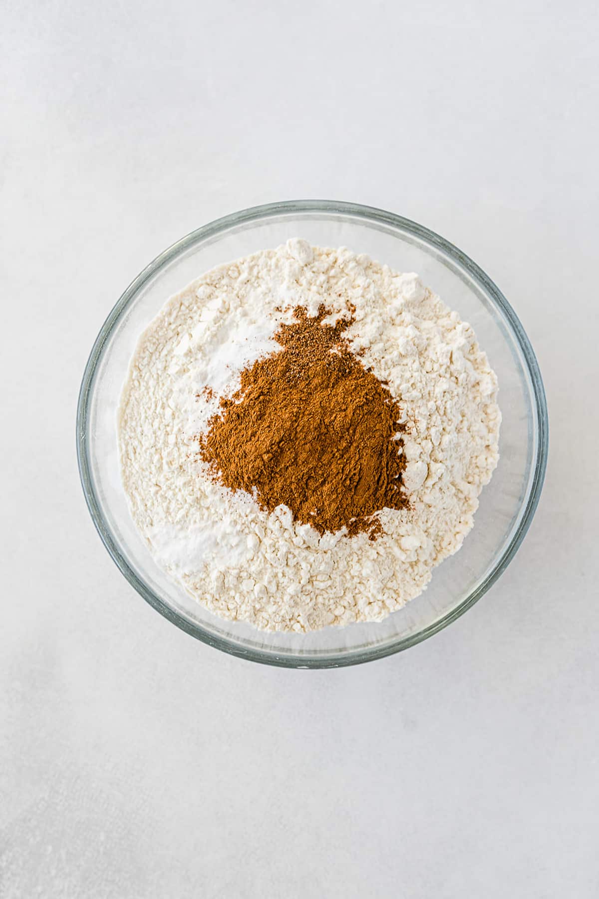Dry ingredients topped with cinnamon and nutmeg being mixed together in a large bowl for chocolate chip zucchini bread.