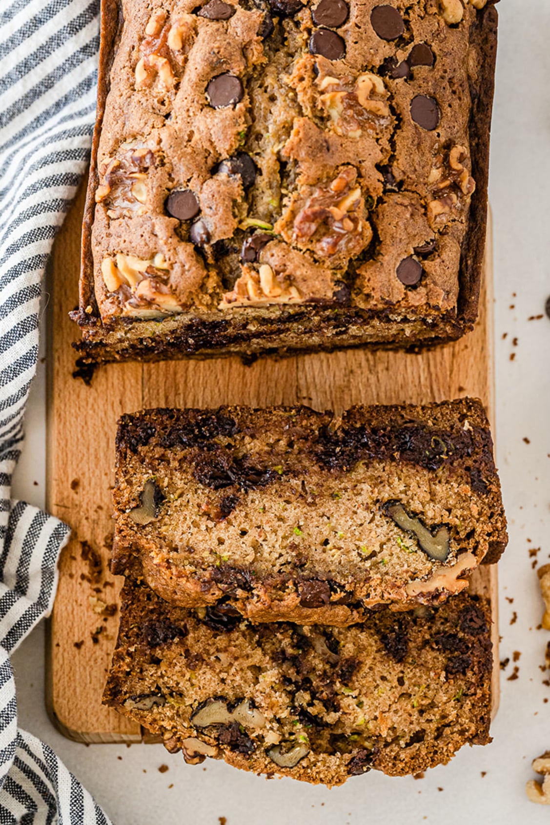Loaf of chocolate chip zucchini bread with walnuts from above on a cutting board with two slices cut from the end.
