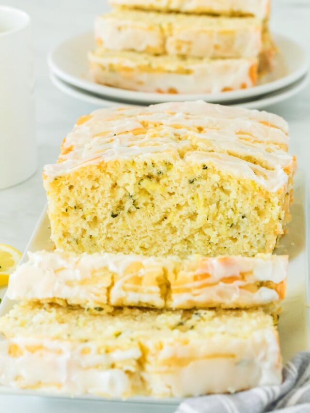 Glazed lemon zucchini loaf cake sliced on a cutting board looking from the end with more slices in the background.
