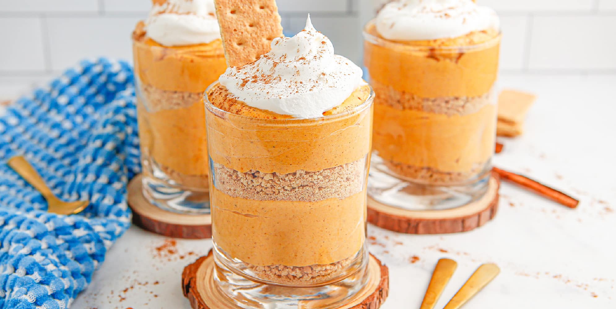 Wide view of three pumpkin desserts in glasses with whipped cream on top.